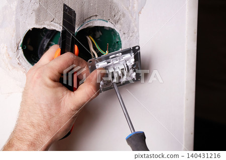 A person is using a screwdriver to install an electrical outlet on a white wall. A person is using a screwdriver to install an electrical outlet on a white wall. 140431216