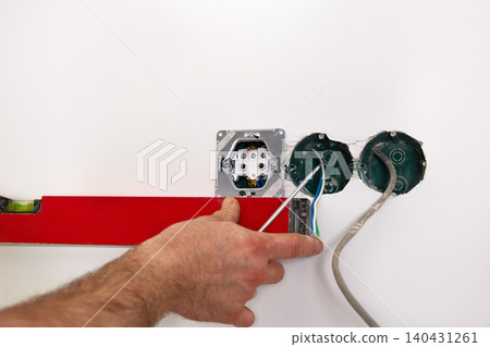 Work on installing electrical sockets. An electrician uses a building level to check that the sockets are level Work on installing electrical sockets. An electrician uses a building level to check that the sockets are level 140431261