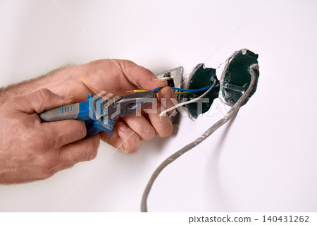 Electrician installs an electrical outlet into a wall using a screwdriver. Electrician installs an electrical outlet into a wall using a screwdriver. 140431262