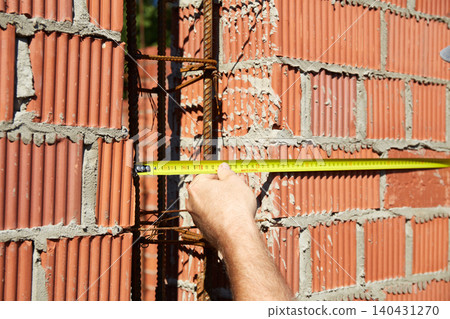 A construction worker is measuring a brick wall at a building site A construction worker is measuring a brick wall at a building site 140431270