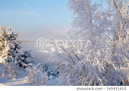 Snowy scene near a river with frost-covered trees and a bridge in the distance during winter Snowy scene near a river with frost-covered trees and a bridge in the distance during winter 140431418