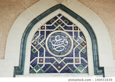 Blue mosaic tile arch with Arabic calligraphy in Uzbekistan. Traditional Islamic geometric ornament decoration on ancient madrasa wall. Central Asian cultural heritage and architecture. Blue mosaic tile arch with Arabic calligraphy in Uzbekistan. Traditional Islamic geometric ornament decoration on ancient madrasa wall. Central Asian cultural heritage and architecture. 140431639