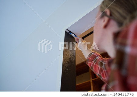 Woman applies dark paint to wall edge with small brush near ceiling Woman applies dark paint to wall edge with small brush near ceiling 140431776