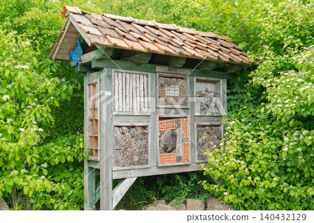 A large handmade wooden insect hotel installed in a green garden near bushes. Promotes biodiversity, organic gardening, wildlife conservation, and eco-friendly environmental protection. Modern bug A large handmade wooden insect hotel installed in a green garden near bushes. Promotes biodiversity, organic gardening, wildlife conservation, and eco-friendly environmental protection. Modern bug 140432129
