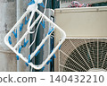 A blue clothespin hanger (corner hanger) hanging in front of the outdoor unit of an air conditioner. 140432210