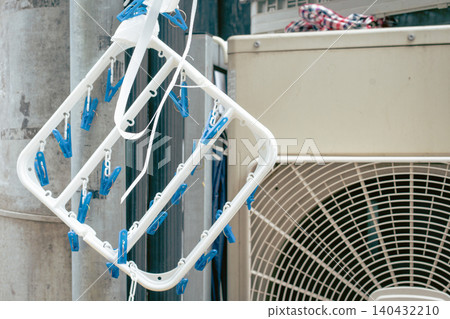 A blue clothespin hanger (corner hanger) hanging in front of the outdoor unit of an air conditioner. A blue clothespin hanger (corner hanger) hanging in front of the outdoor unit of an air conditioner. 140432210
