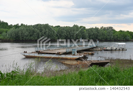 A pontoon bridge spanning a river with banks A pontoon bridge spanning a river with banks 140432543