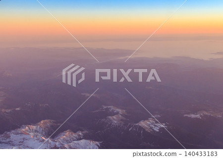 View out of an airplane window of a snow-covered mountain range at sunset View out of an airplane window of a snow-covered mountain range at sunset 140433183