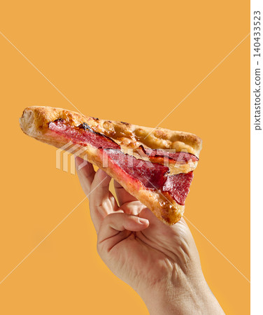 Hand Holding a Slice of Pepperoni Salami Pizza on Bright Yellow Background Hand Holding a Slice of Pepperoni Salami Pizza on Bright Yellow Background 140433523