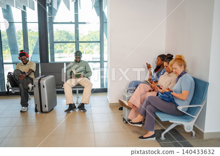 Diverse people waiting at airport terminal using technology and reading Diverse people waiting at airport terminal using technology and reading 140433632