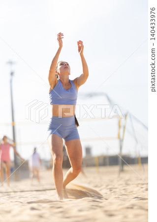 Young woman practices beach volleyball while others play in sunny day at sandy court near ocean 140433976