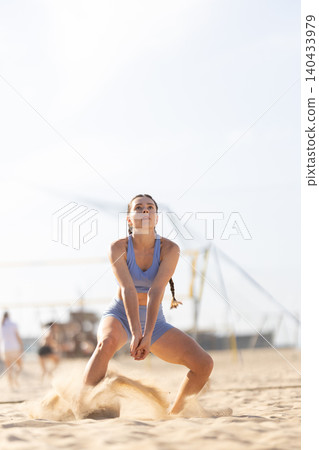 Woman plays volleyball on the beach during a sunny day while sand rises around her Woman plays volleyball on the beach during a sunny day while sand rises around her 140433979