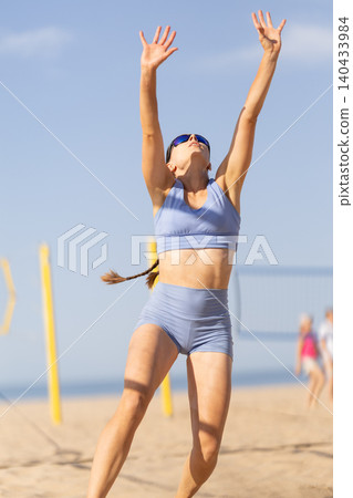 Woman plays beach volleyball during the day near the ocean with other players in the background Woman plays beach volleyball during the day near the ocean with other players in the background 140433984