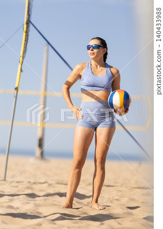 Woman plays beach volleyball in summer with blue sky and sandy court in the background near ocean waves Woman plays beach volleyball in summer with blue sky and sandy court in the background near ocean waves 140433988