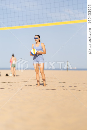 Woman plays beach volleyball while wearing sunglasses on a sandy beach during a sunny day Woman plays beach volleyball while wearing sunglasses on a sandy beach during a sunny day 140433993
