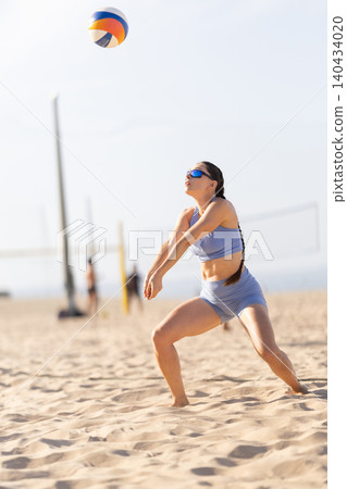 Female player hits volleyball on beach sand during a sunny day with nets and other players in the background Female player hits volleyball on beach sand during a sunny day with nets and other players in the background 140434020