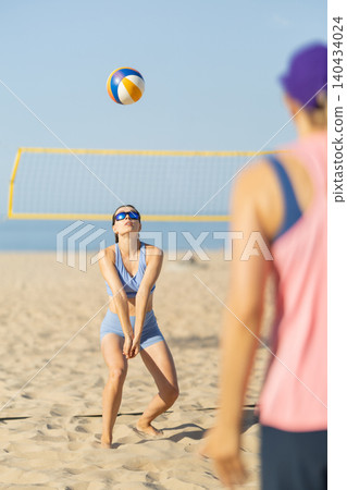 Beach volleyball game takes place on sandy shore under clear blue sky in the late morning with players ready to serve and receive the ball Beach volleyball game takes place on sandy shore under clear blue sky in the late morning with players ready to serve and receive the ball 140434024