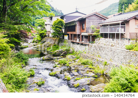 A rural landscape where the gentle murmur of a clear stream harmonizes with traditional Japanese houses. 140434764