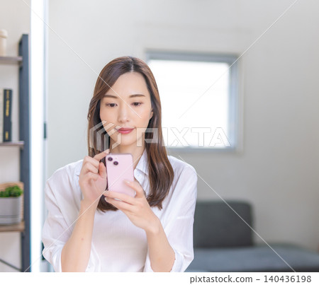 A smiling woman using her smartphone indoors. A smiling woman using her smartphone indoors. 140436198