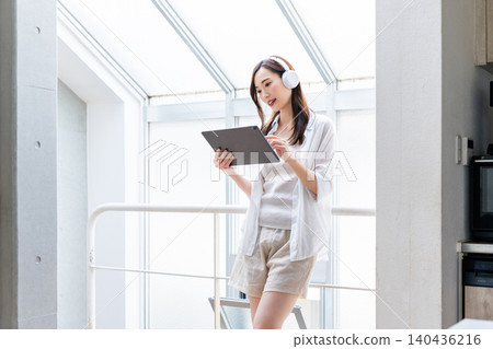 A woman wearing headphones and operating a tablet. A woman wearing headphones and operating a tablet. 140436216