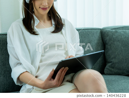 一位女士正坐在沙發上使用平板電腦。 140436228