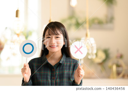 一位微笑的女子雙手拿著○×符號。 140436456