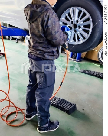 一名修理工在修理店裡穿著圍裙，用工具更換輪胎和輪轂，這是他的背影。 140437407
