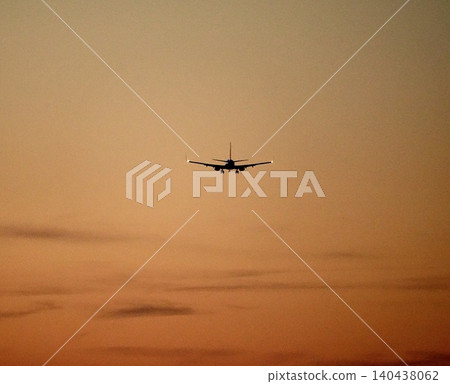 A scene of an airplane preparing to land, flying through the crimson twilight sky. A scene of an airplane preparing to land, flying through the crimson twilight sky. 140438062
