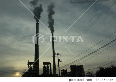 A city awakens, and smoke wafts. The industrial complex, illuminated by the morning light, poses a question about the future of the Earth. A city awakens, and smoke wafts. The industrial complex, illuminated by the morning light, poses a question about the future of the Earth. 140438856