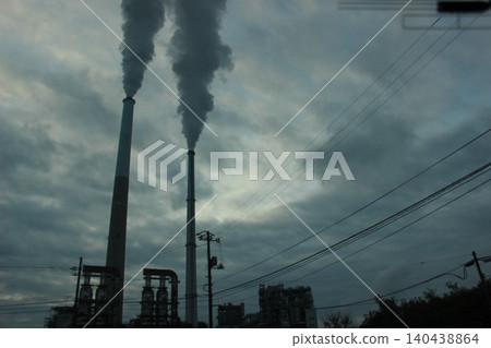 A city awakens, and smoke wafts. The industrial complex, illuminated by the morning light, poses a question about the future of the Earth. A city awakens, and smoke wafts. The industrial complex, illuminated by the morning light, poses a question about the future of the Earth. 140438864
