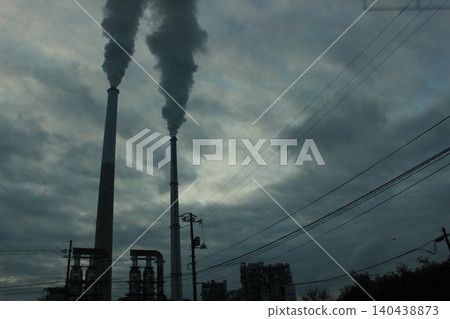 A city awakens, and smoke wafts. The industrial complex, illuminated by the morning light, poses a question about the future of the Earth. A city awakens, and smoke wafts. The industrial complex, illuminated by the morning light, poses a question about the future of the Earth. 140438873