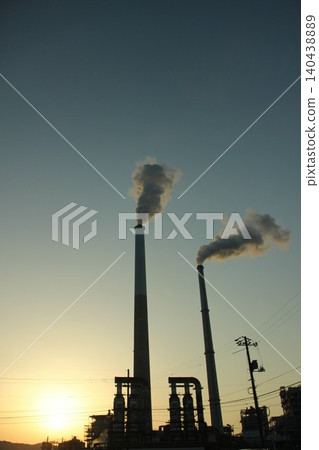 A city awakens, and smoke wafts. The industrial complex, illuminated by the morning light, poses a question about the future of the Earth. A city awakens, and smoke wafts. The industrial complex, illuminated by the morning light, poses a question about the future of the Earth. 140438889