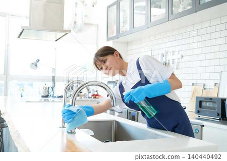 A female staff member meticulously disinfects and cleans the kitchen sink. A female staff member meticulously disinfects and cleans the kitchen sink. 140440492