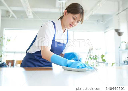 A young female cleaning staff member wipes down the kitchen counter. A young female cleaning staff member wipes down the kitchen counter. 140440501