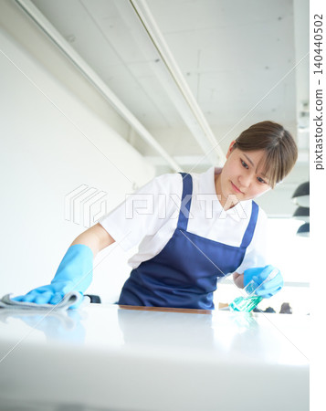 A young female cleaning staff member wipes down the kitchen counter. A young female cleaning staff member wipes down the kitchen counter. 140440502