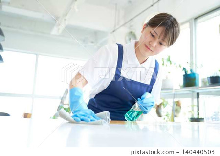 A young female cleaning staff member wipes down the kitchen counter. 140440503