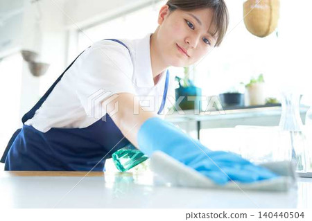 A young cleaning staff member wipes down the counter. 140440504