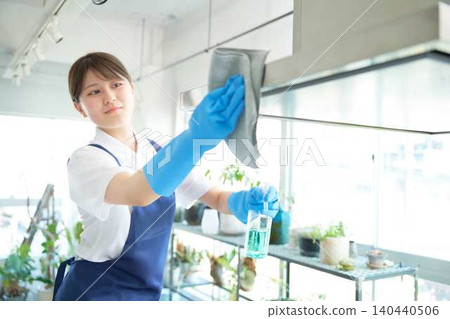 A female cleaning staff member wipes away grease from the range hood in the kitchen. A female cleaning staff member wipes away grease from the range hood in the kitchen. 140440506