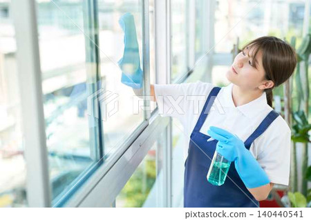 A young cleaning staff member wipes down the office windows. A young cleaning staff member wipes down the office windows. 140440541