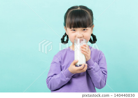 Little Asian girl drinking a glass of fresh milk for calcium and healthy growth, mint green background. 140440830