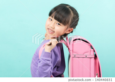 A happy little girl with a pink backpack smiles at the camera. 140440831