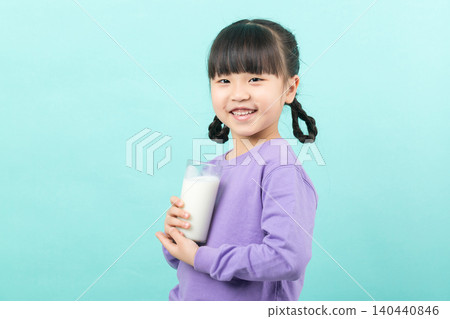 Little Asian girl drinking a glass of fresh milk for calcium and healthy growth, mint green background. 140440846