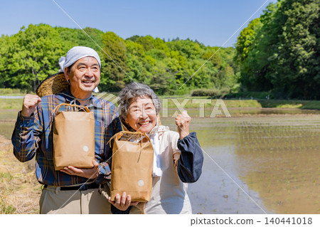 一對老年夫婦手捧收穫的農產品，面帶笑容，做出勝利的手勢。 140441018