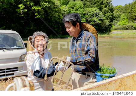 A smiling senior couple and farming tools are preparing for rice planting. A smiling senior couple and farming tools are preparing for rice planting. 140441040