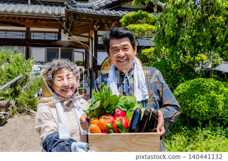 A Japanese senior farming couple holding freshly harvested vegetables A Japanese senior farming couple holding freshly harvested vegetables 140441132