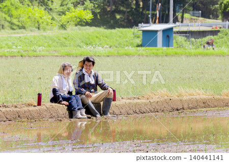 A senior couple resting on a path between rice paddies. A senior couple resting on a path between rice paddies. 140441141