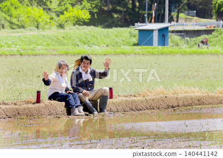 A smiling senior couple waving during a break from rice planting work. A smiling senior couple waving during a break from rice planting work. 140441142