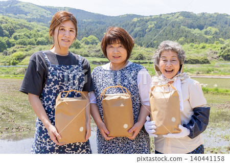 Three generations of Japanese women smile in a rice field, holding harvested produce. Three generations of Japanese women smile in a rice field, holding harvested produce. 140441158
