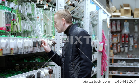 A man in a hardware store, choosing sockets and switches. Customer selects a new electrical socket in a hardware store, standing in an aisle and examining the item in his hand A man in a hardware store, choosing sockets and switches. Customer selects a new electrical socket in a hardware store, standing in an aisle and examining the item in his hand 140441207