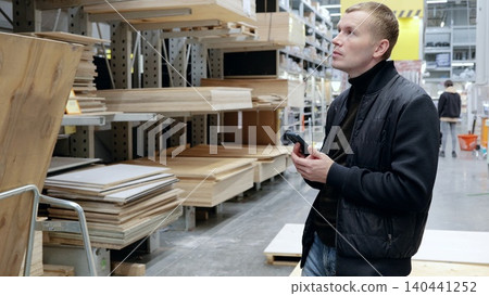 Man comparing wood panels on smartphone at hardware store, choosing best quality for diy project. Busy warehouse store with customers, focusing on craftsmanship and home improvement Man comparing wood panels on smartphone at hardware store, choosing best quality for diy project. Busy warehouse store with customers, focusing on craftsmanship and home improvement 140441252